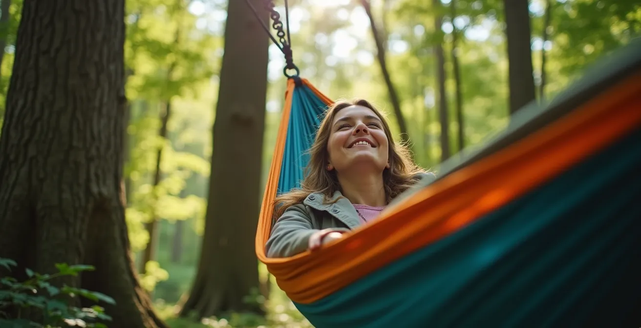 A person relaxing peacefully in a hammock strung between two trees in a sun-dappled forest.